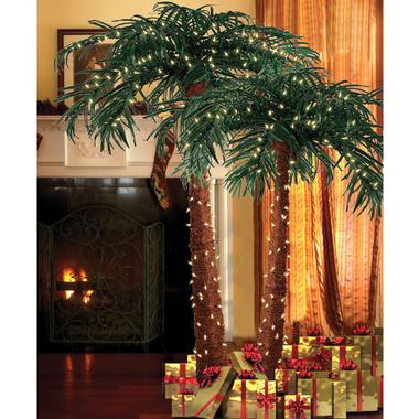 Natural palm trees decorated with Christmas lights and wrapped gifts underneath, on display next to a roaring fireplace